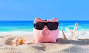 A piggy bank with sunglasses on a beach.