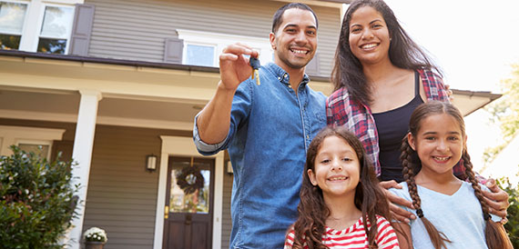 Family smiling in front of their new house.