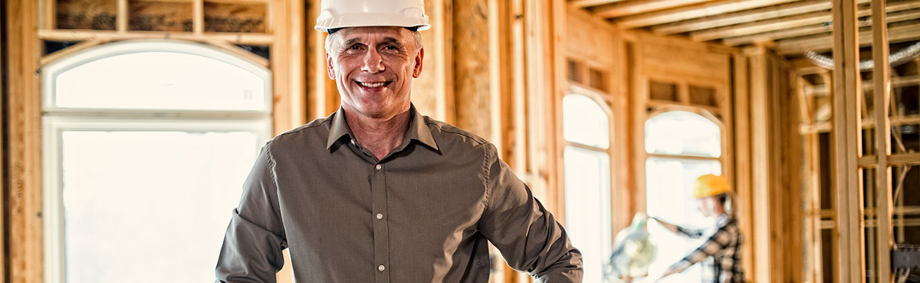 Man in a house under construction wearing a hard hat. 