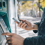 A man on his phone using an ATM to withdraw finances.