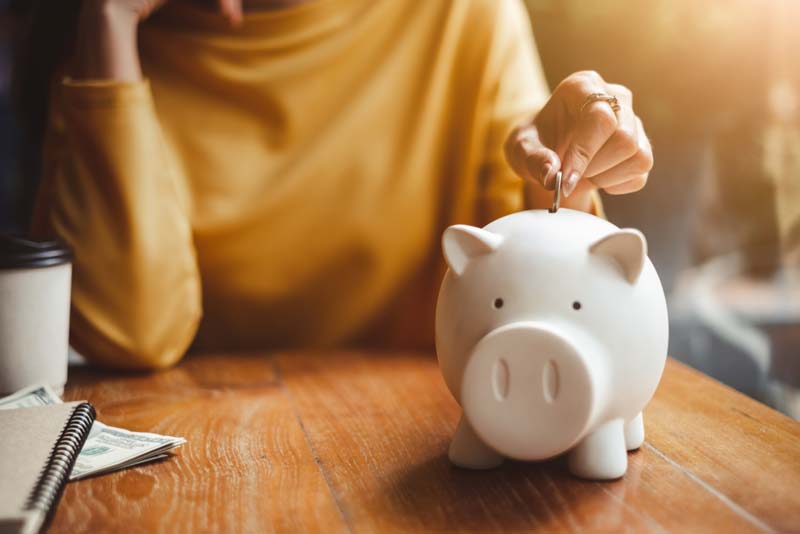 A woman putting a coin into a piggy bank.