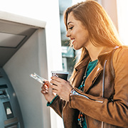 A man on his phone using an ATM to withdraw finances.